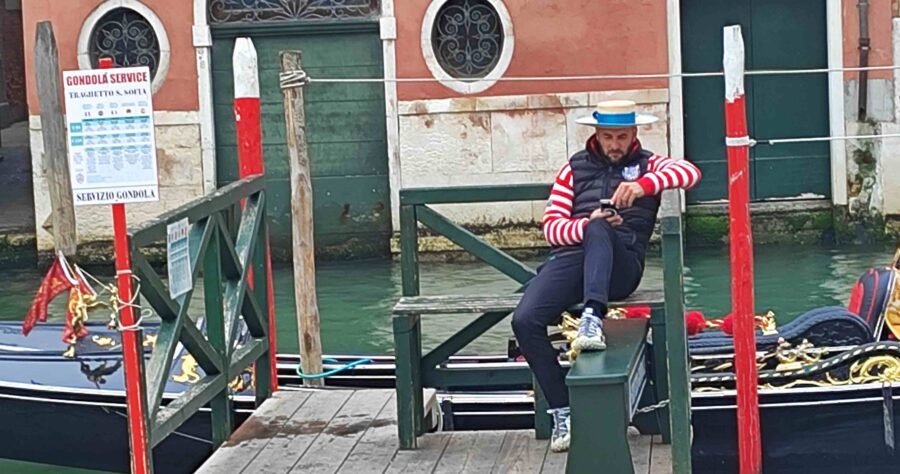 Gondoliere in gestreifter Kleidung sitzt auf einer Holzbank am Kanal in Venedig.